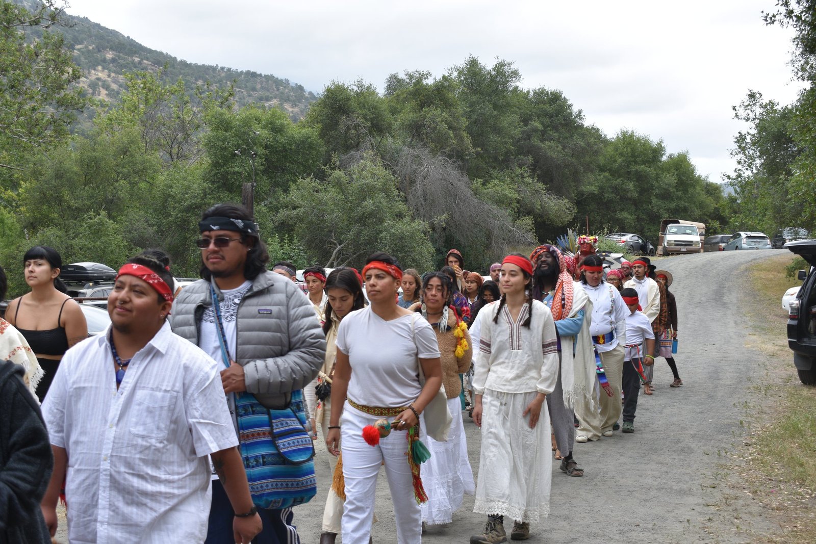 Community members walking together in ceremony among wooded hills.